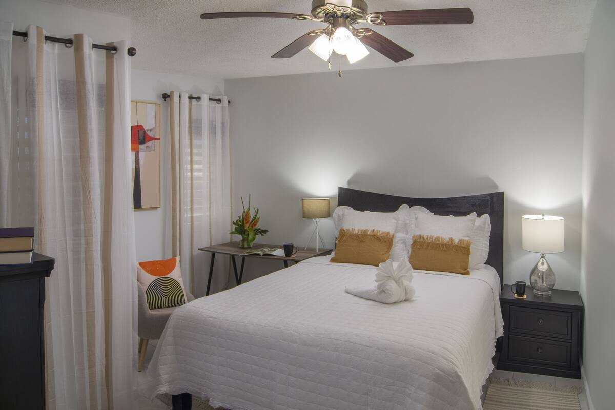 A neatly arranged hotel room with a bed, bedside tables, a ceiling fan, and a nightstand with a lamp.