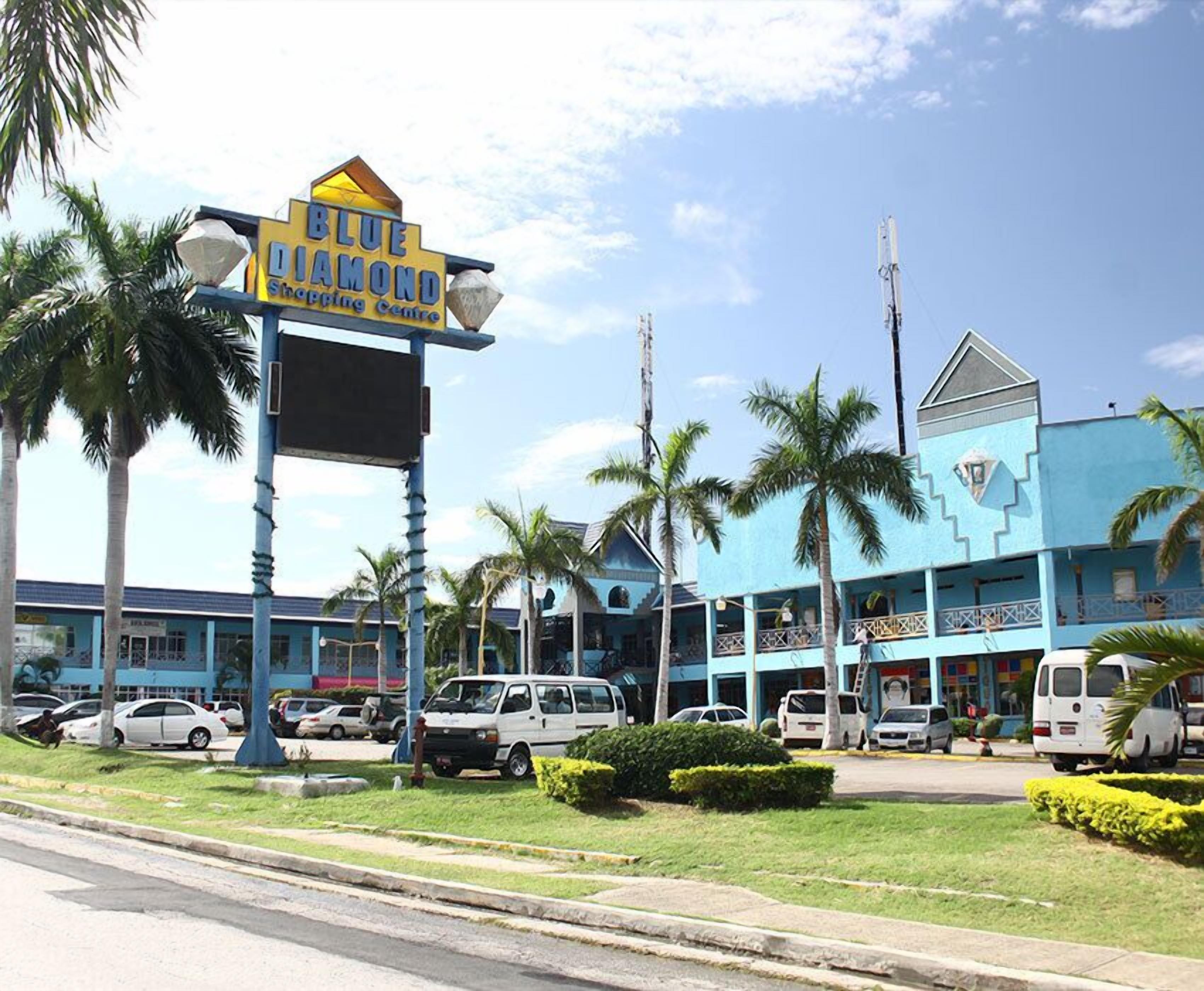 A Blue Diamond Shopping Centre with a prominent sign, surrounded by palm trees and parked vehicles.