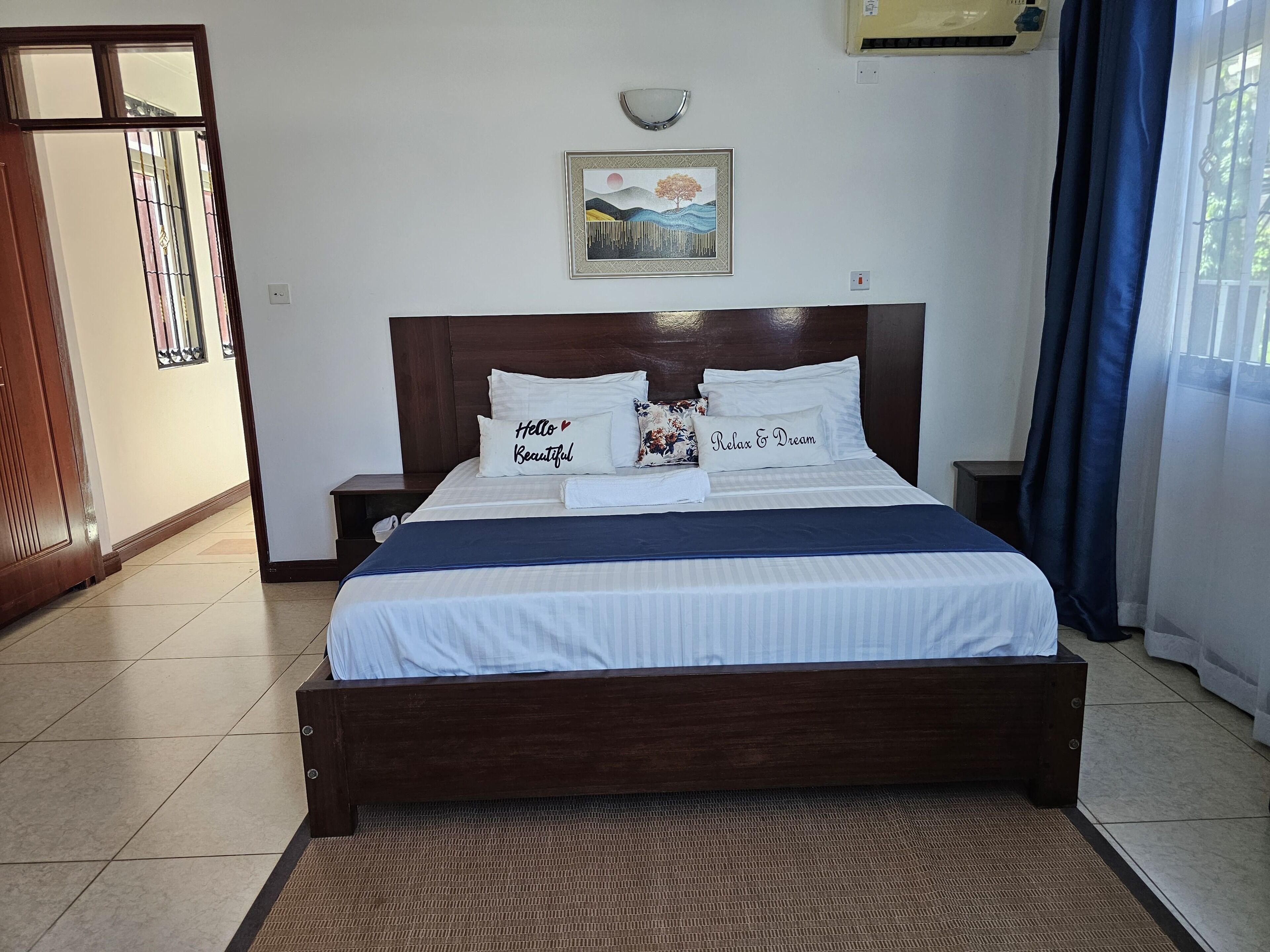 A neatly made bed with pillows, a framed picture above it, and a window with curtains.