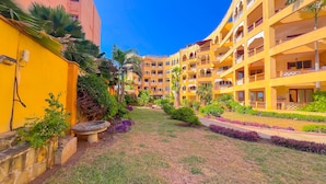 Une cour intérieure avec un bâtiment jaune doté de balcons et un jardin où poussent différentes espèces de plantes.