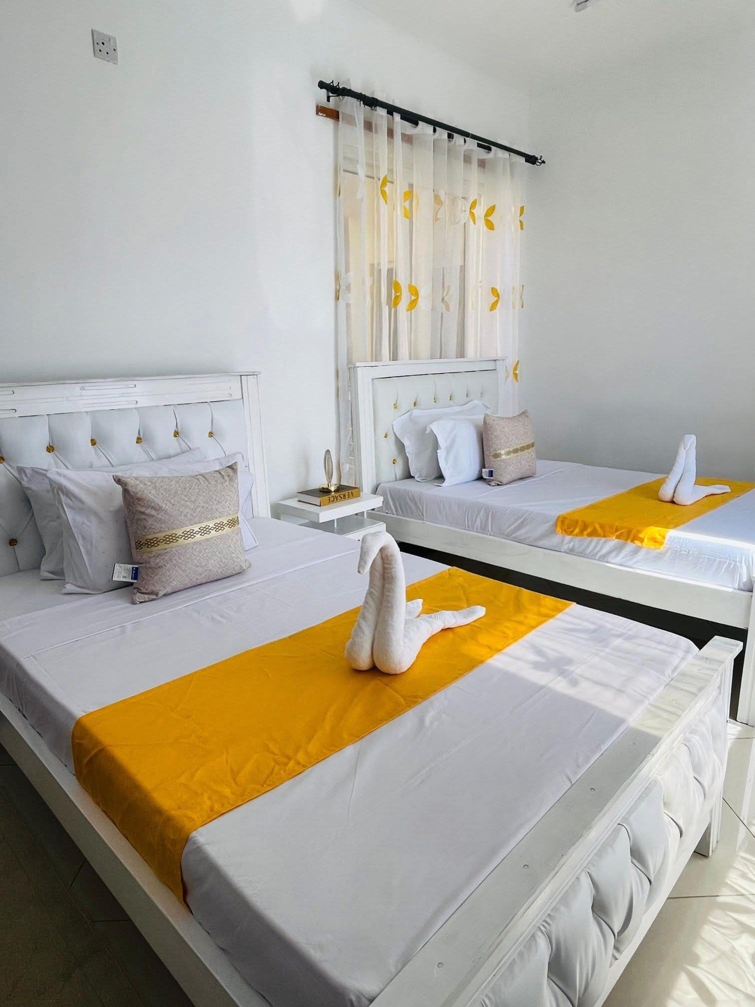 A hotel room with two beds, each with white bedding and a yellow accent.