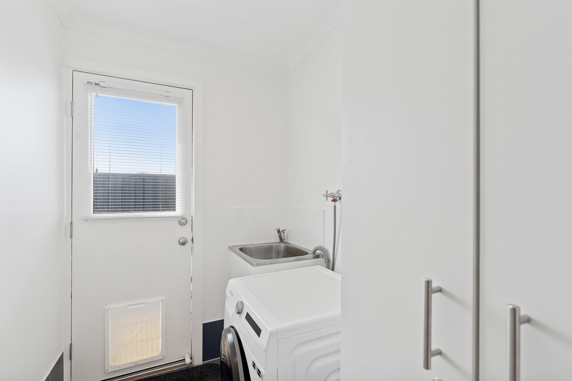 A compact laundry room with a washing machine, a sink, and a window with blinds.