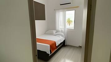 Un dormitorio con cama, ventana con cortinas y un equipo de aire acondicionado.