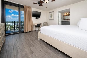 Habitación de hotel con una cama grande, un escritorio, un televisor, un ventilador de techo y un balcón con vistas.