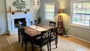 A dining room with a brick fireplace, a chandelier, and a view of the outdoors through a window. - Quiet Mid-Mod Getaway with Hot Tub, Outdoor Seating & Firepit (Asheville)