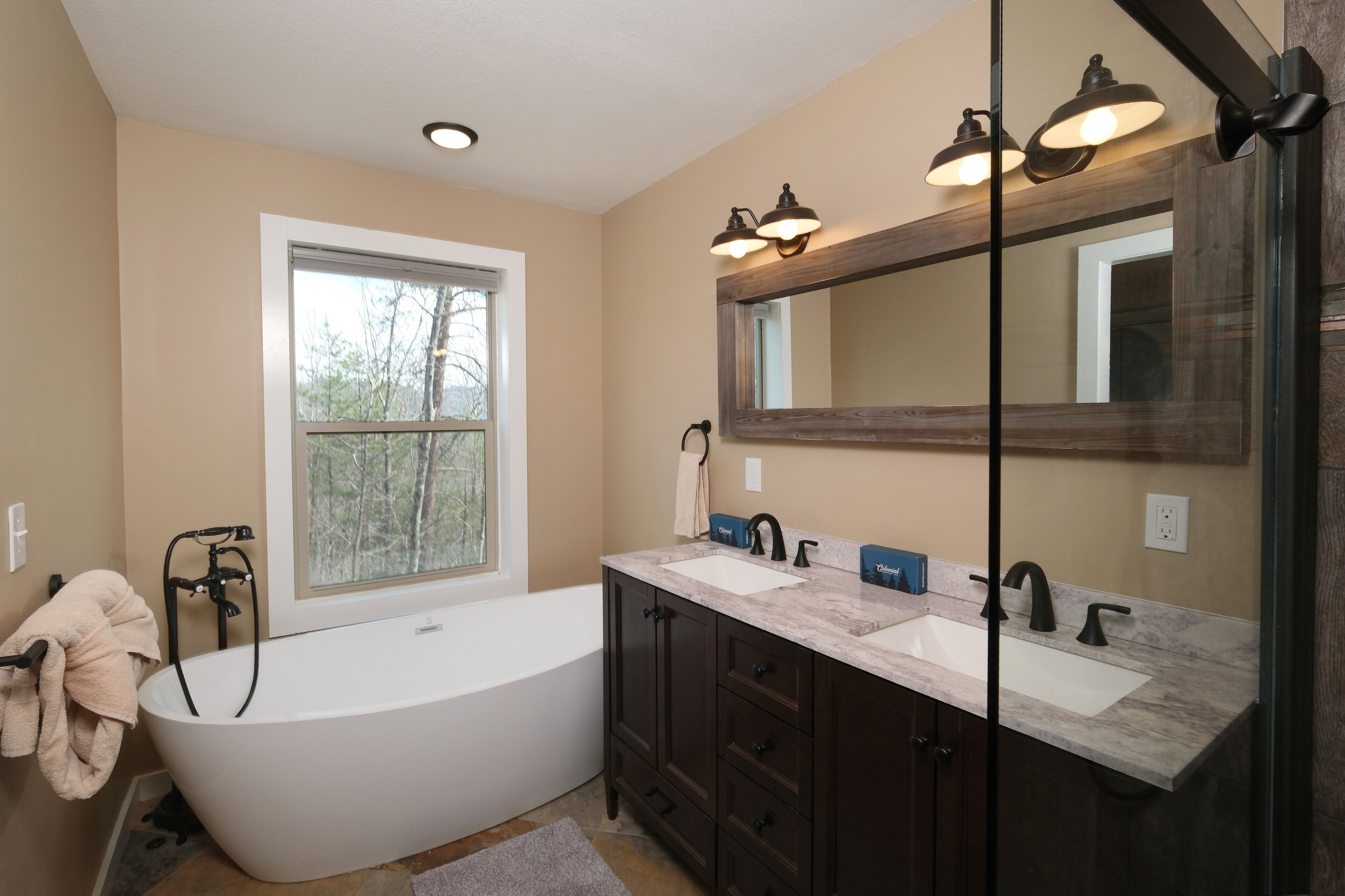 A modern bathroom with a freestanding bathtub, dual sinks, dark wooden cabinets, and a large mirror.