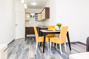 A modern kitchen with a dining area, featuring a white door, brown cabinets, and a table with yellow chairs. - Limunada Apartments (Utjeha)