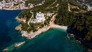 An aerial view of a coastal property with a large white building surrounded by lush greenery and clear turquoise waters. - Limunada Apartments (Utjeha)