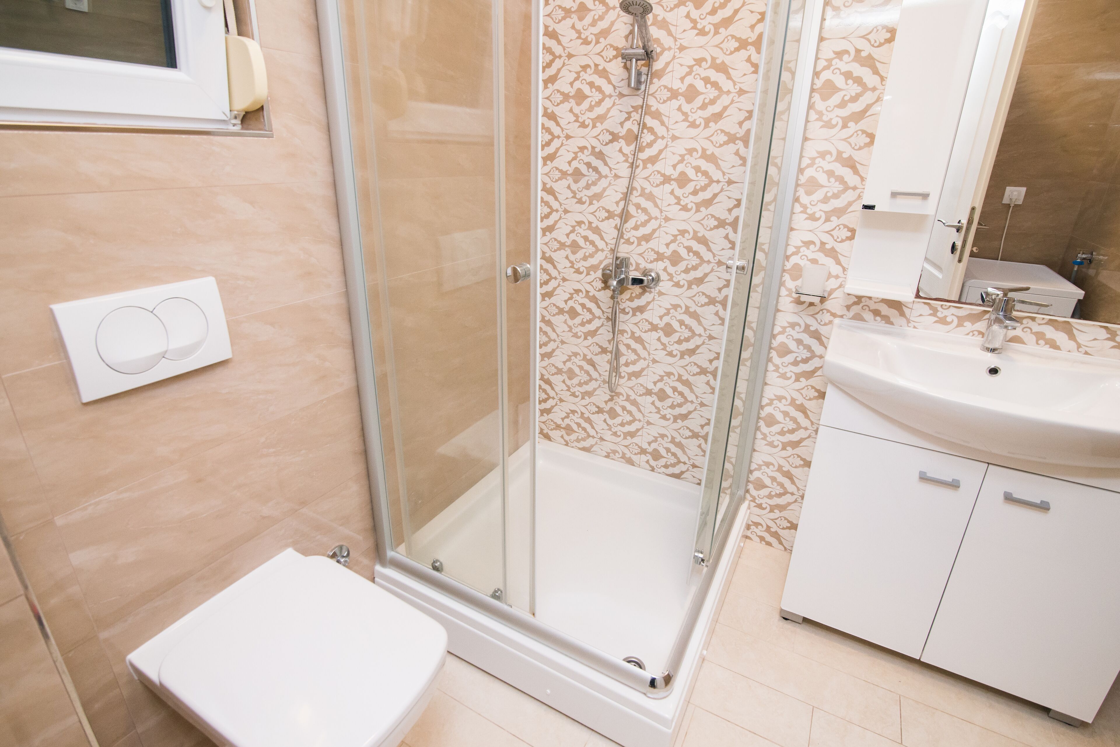 A bathroom with a glass shower enclosure, a toilet, a sink, and a cabinet.