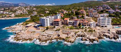 A coastal town with buildings along the shoreline, rocky terrain, and clear blue waters.