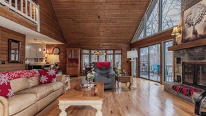 Ein geräumiges Wohnzimmer mit Holzböden, einem Kamin, einer Couch mit roten Kissen und einem Esstisch.