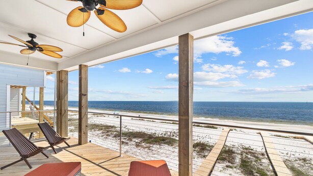 A covered deck with wooden pillars, lounge chairs, and a view of the beach and ocean.