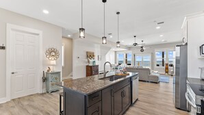 A spacious kitchen with a central island, pendant lighting, and a view to the living area.