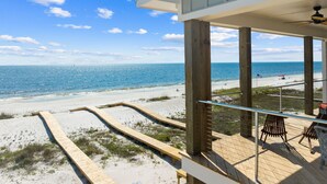 A beach view from a wooden deck with a railing, overlooking a sandy beach and the ocean.
