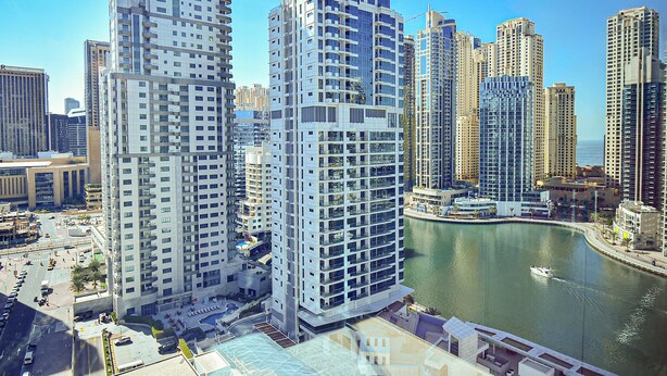 A high-rise building with multiple floors, a waterfront view, and a marina with boats. - Budget 1BR Apt in Marina  -Time (Dubai)
