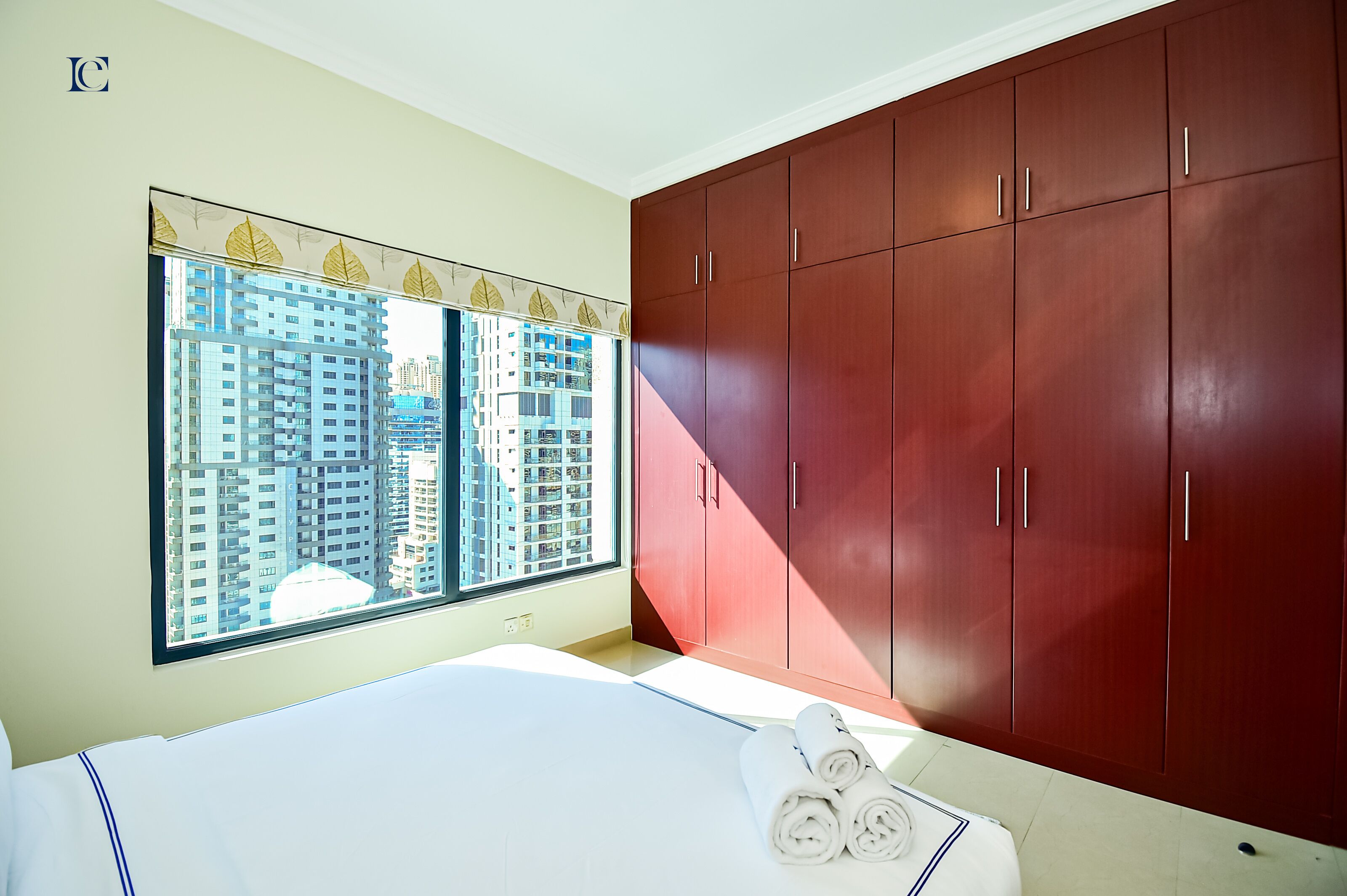 A bedroom with a large window, a bed, and a wardrobe.