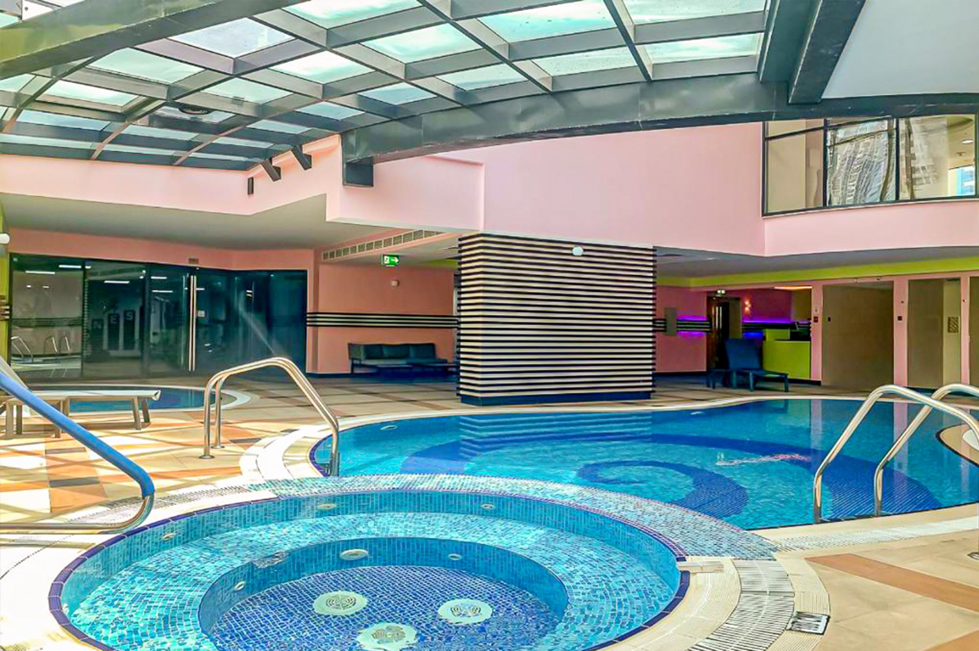 An indoor swimming pool with a glass ceiling, a reception area, and a seating area.