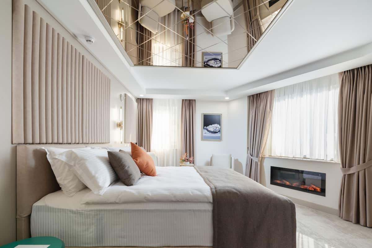 A modern bedroom with a large bed, a small table, a fireplace, and a view of the city through the window.