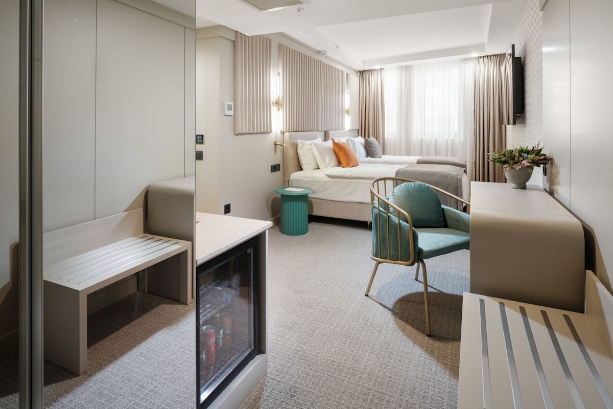 A modern hotel room with a bed, a desk, a chair, a TV, and a window.