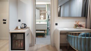 Habitación de hotel moderna con kitchenette, un refrigerador pequeño, un escritorio con silla, un espejo grande y vistas al baño.