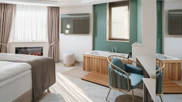A modern hotel room with a bed, a seating area with a chair, a small table, a bathtub, and a mirror.