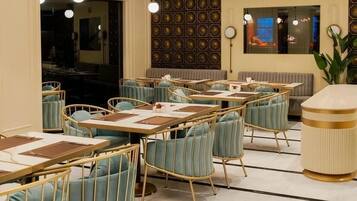 Un restaurante con mesas redondas, sillas con cojines azules y una araña.