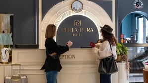 Mostrador de recepción del Hotel Perla Pura con un reloj, una señalización y una araña colgante.
