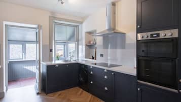 A modern kitchen with black cabinets, a stainless steel range hood, a double oven, and a large window providing natural light.