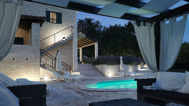 Zona junto a la piscina con sillones reclinables, una mesa de madera y una escalera que sube a un nivel superior.