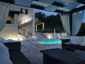 A poolside area with lounge chairs, a wooden table, and a staircase leading to an upper level. - Villa Paradiso (Policnik)