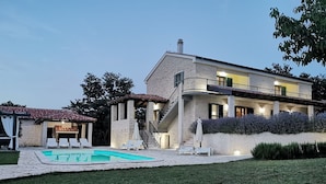 Una casa de dos pisos con piscina, mobiliario exterior y una escalera que sube al nivel superior.