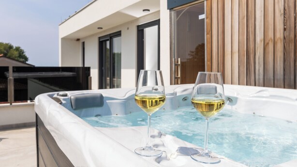 En modern utomhusbubbelpool med två glas vitt vin.