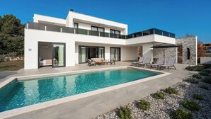 Ett modernt hus i två våningar med en swimmingpool, en uteplats och en mur av sten.