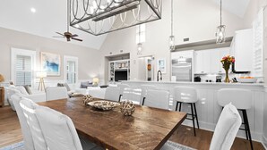 Une cuisine moderne avec des meubles blancs, une table à manger en bois et des luminaires suspendus.