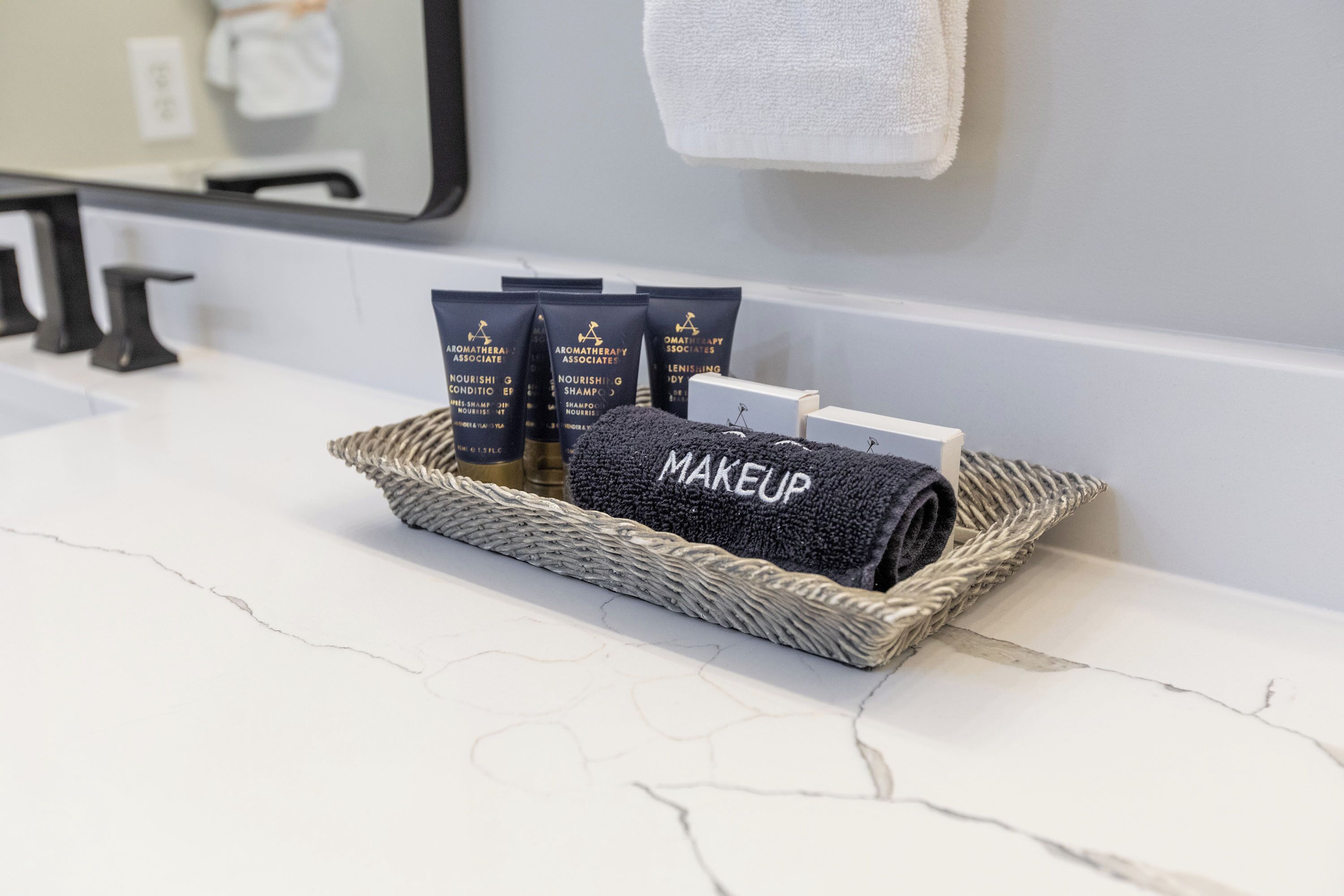 A bathroom vanity with a marble countertop, a woven basket containing toiletries, and a towel hanging on the wall.