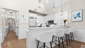 Une cuisine moderne avec des meubles blancs, des appareils en acier inoxydable et un îlot central doté de tabourets de bar.