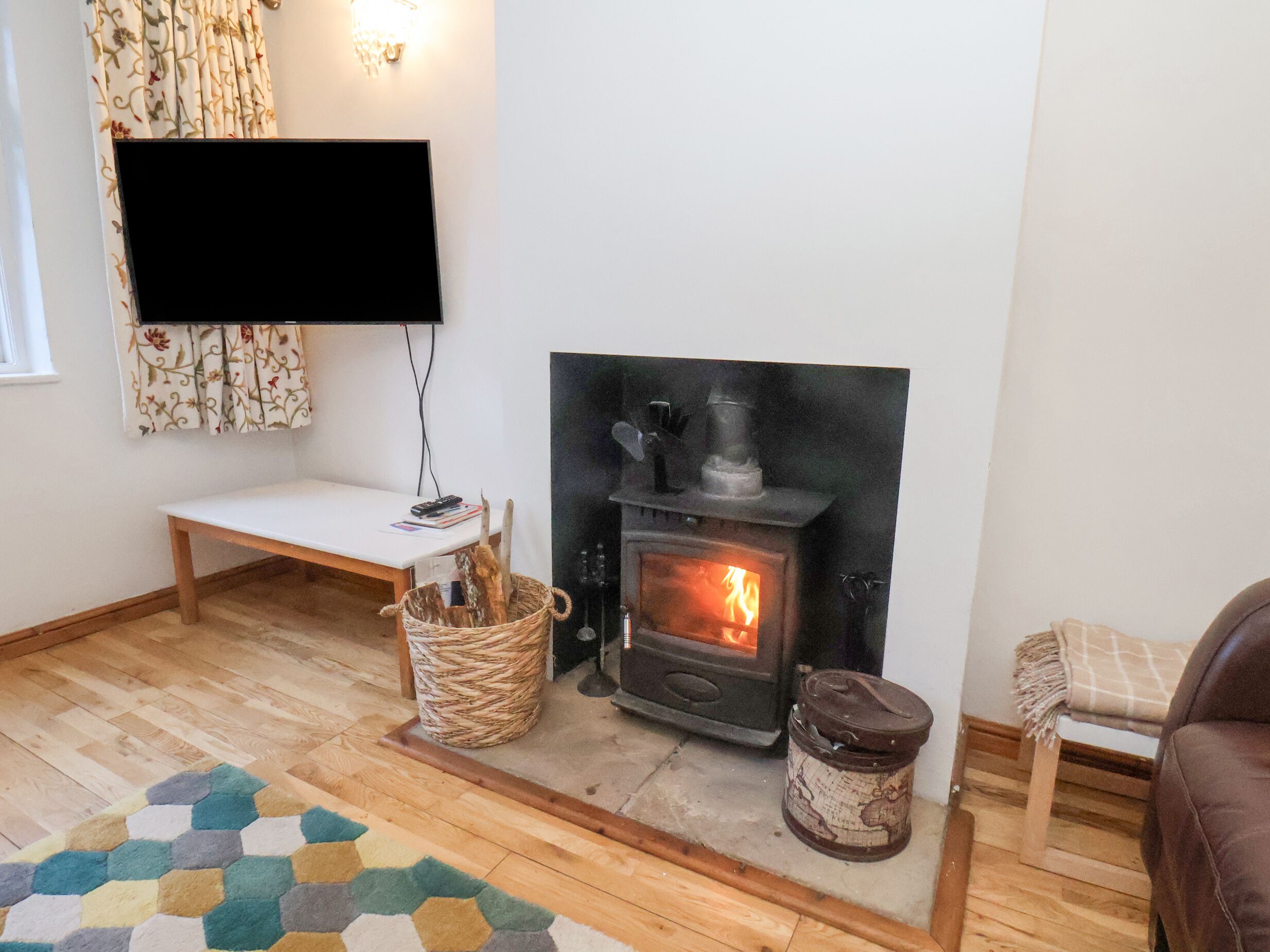 Una sala de estar acogedora con chimenea, televisor montado en la pared, un banco de madera y una alfombra estampada.