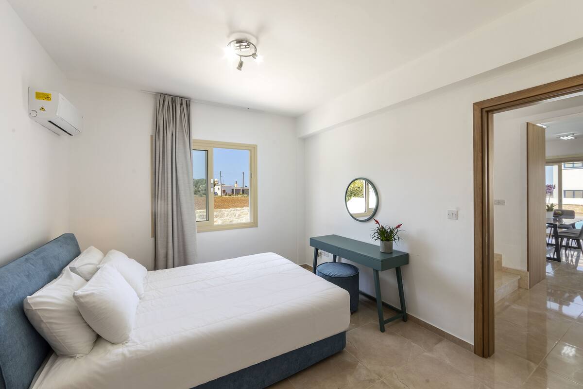 Quarto com cama, escrivaninha, espelho e janela.