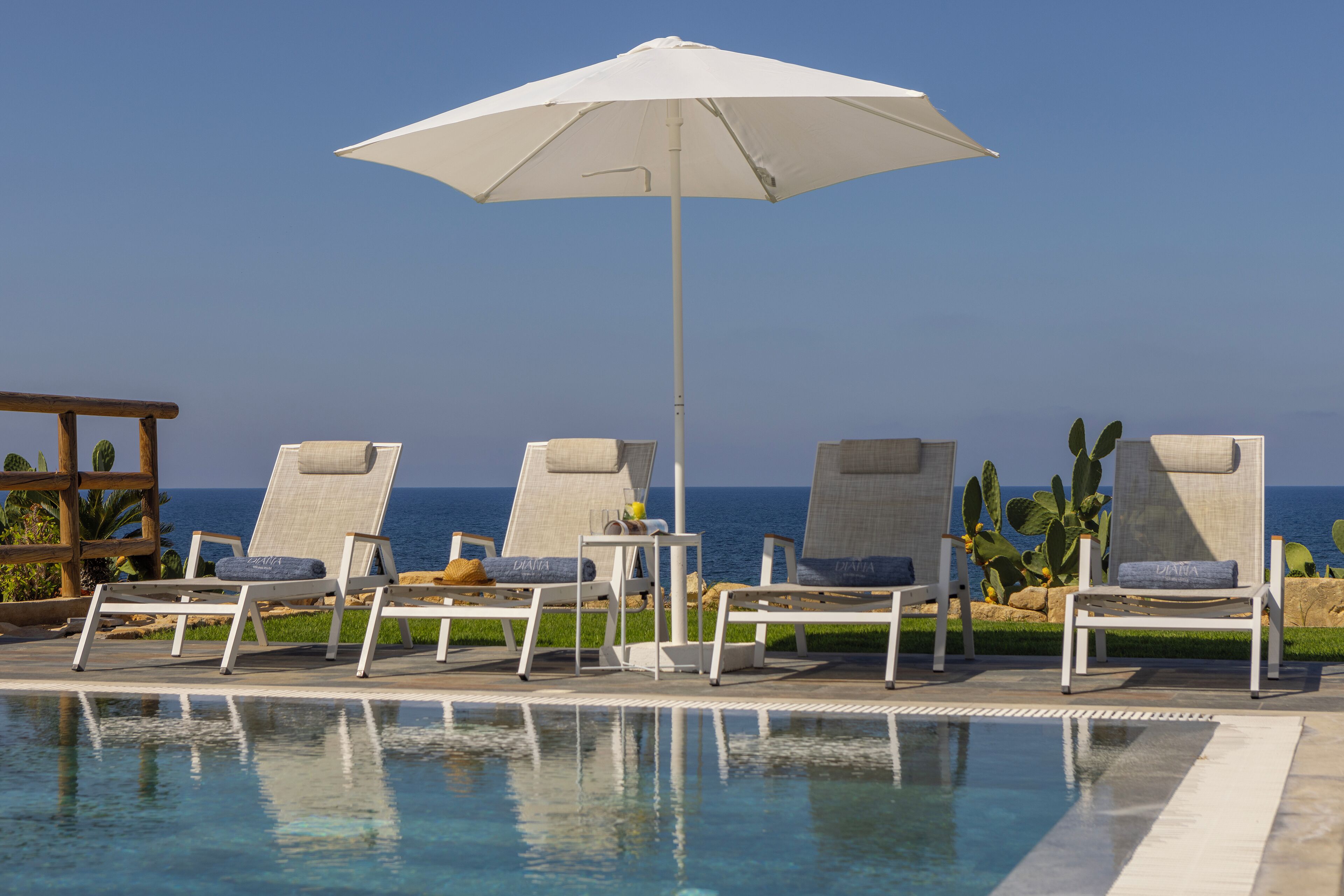 Zona junto a la piscina con sillones de descanso y un amplio paraguas, con vista al mar.