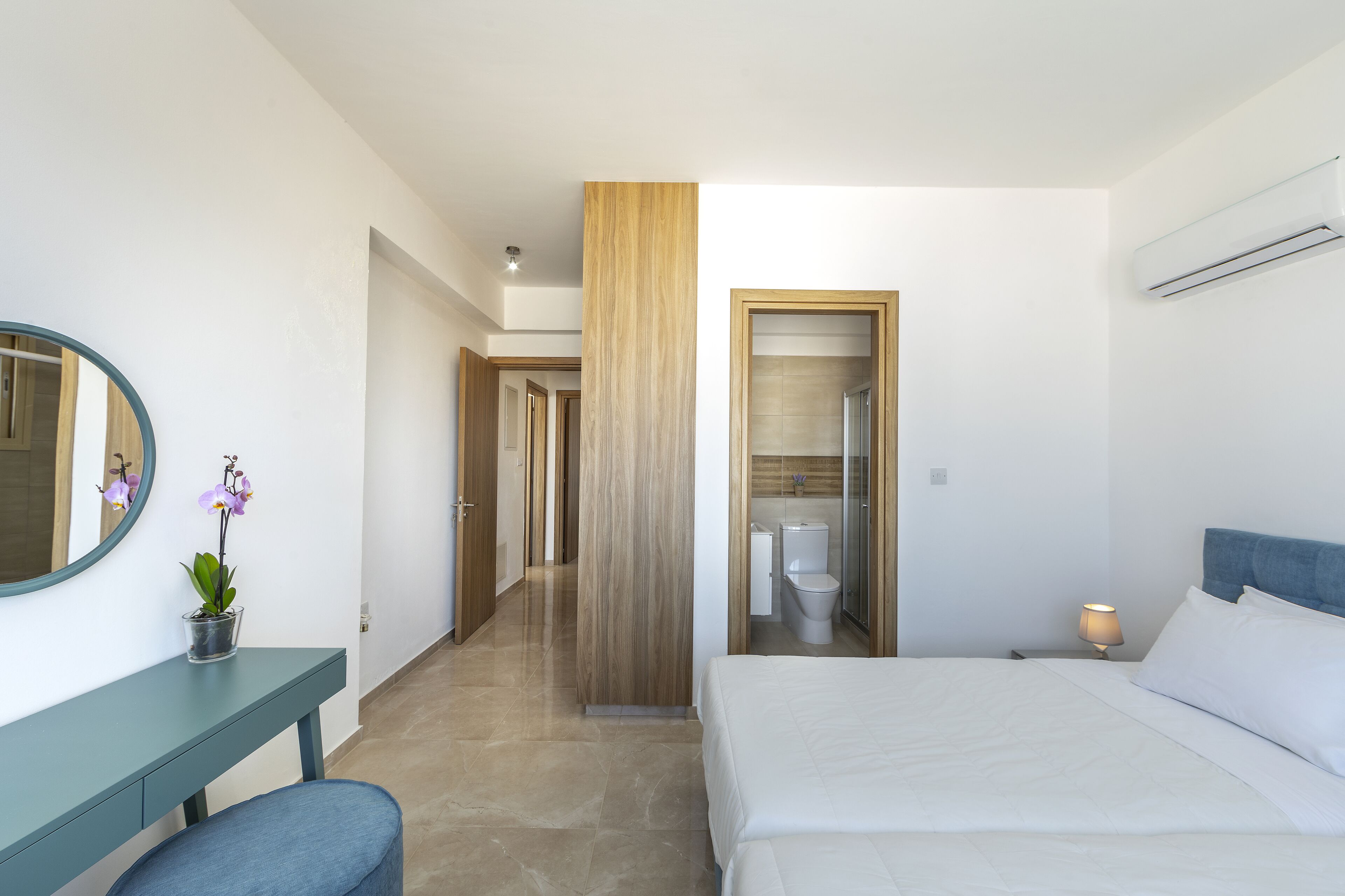 A modern hotel room with a bed, bedside table, and a mirror. There is a bathroom with a toilet and a shower.