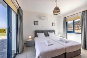 Un lit double avec deux oreillers, une table de chevet avec une lampe, un climatiseur fixé au mur et une grande fenêtre avec des rideaux.