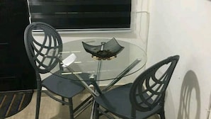 Ett litet glasbord med två stolar, en svart dörr och ett fönster med persienner.