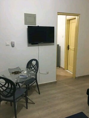 Ein Essbereich mit einem Glastisch und Stühlen, einem an der Wand befestigten Flachbildfernseher und einer Tür zu einem anderen Raum.