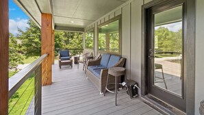 A covered outdoor deck with wicker furniture, a sofa, and a bar stool. - Richland Chambers Lakefront 2-story home with boat dock and pavilions. (Streetman)