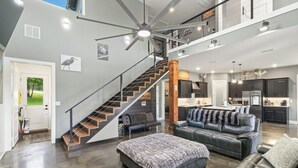A spacious living area with a staircase, a large sofa, and a kitchen in the background. - Richland Chambers Lakefront 2-story home with boat dock and pavilions. (Streetman)