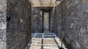 A narrow stone corridor with a wooden ceiling and a metal pipe running along the wall.