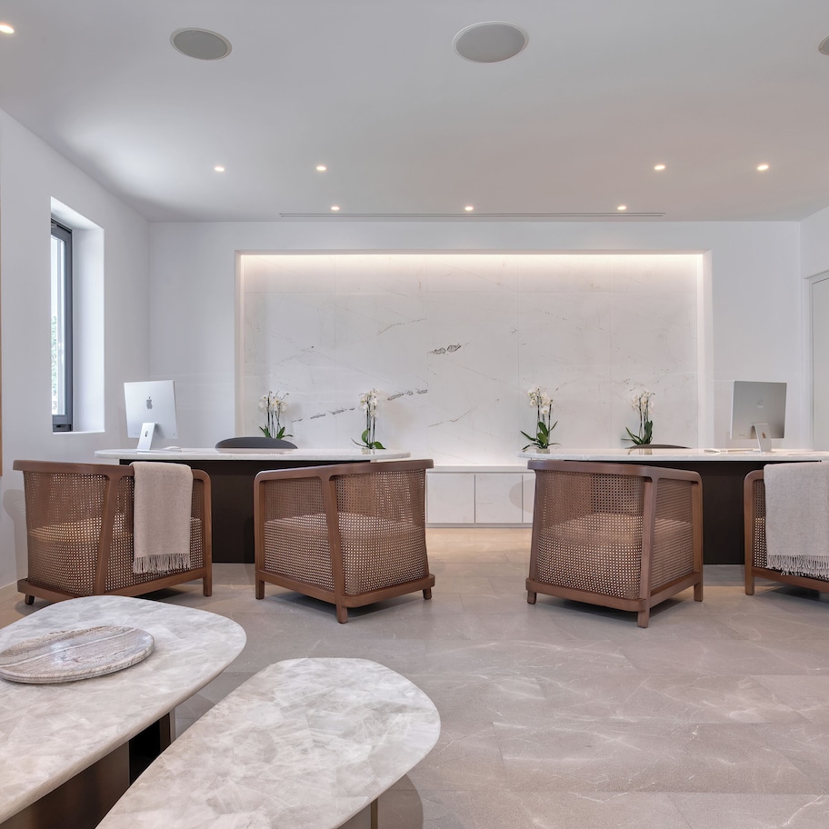 A modern, minimalist reception area with a marble reception desk, wicker chairs, and a large abstract painting on the wall.