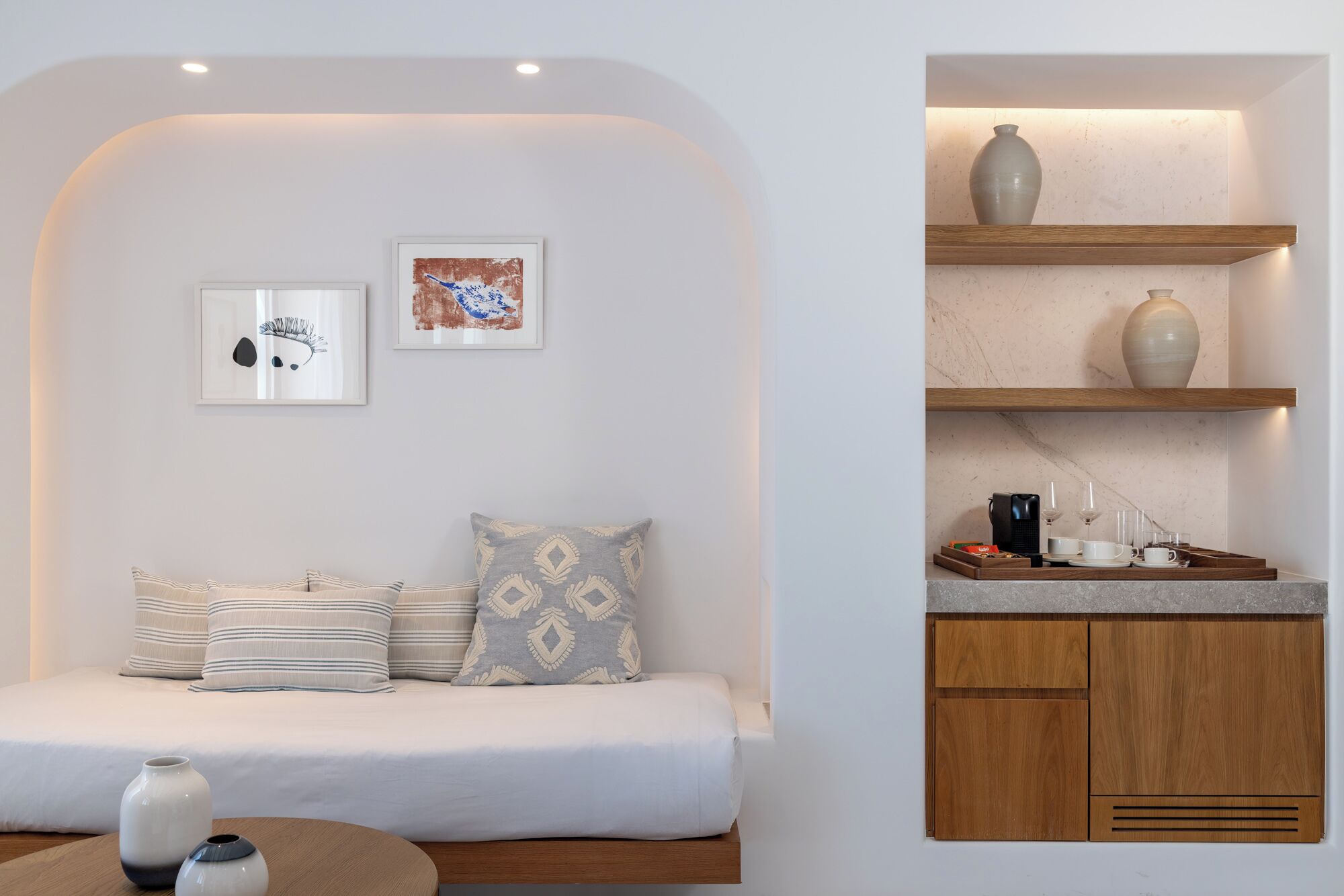 Une chambre moderne comprenant un lit, deux œuvres d’art encadrées et un coin cuisine avec un meuble en bois et une étagère.