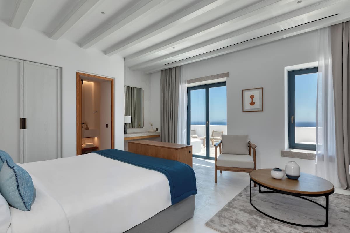 A modern hotel room with a large bed, a wooden desk, a seating area, and a balcony with a view.