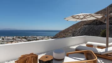Une terrasse sur le toit, dotée d’une balustrade blanche, de chaises longues, d’une table en bois et offrant une vue sur la mer et la ville au loin.